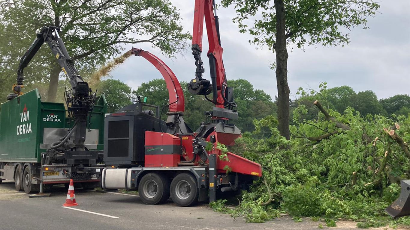 The 952 mega chipper cutting tree limbs and spraying woodchips into a large dumpster trailer along a heavily wooded area