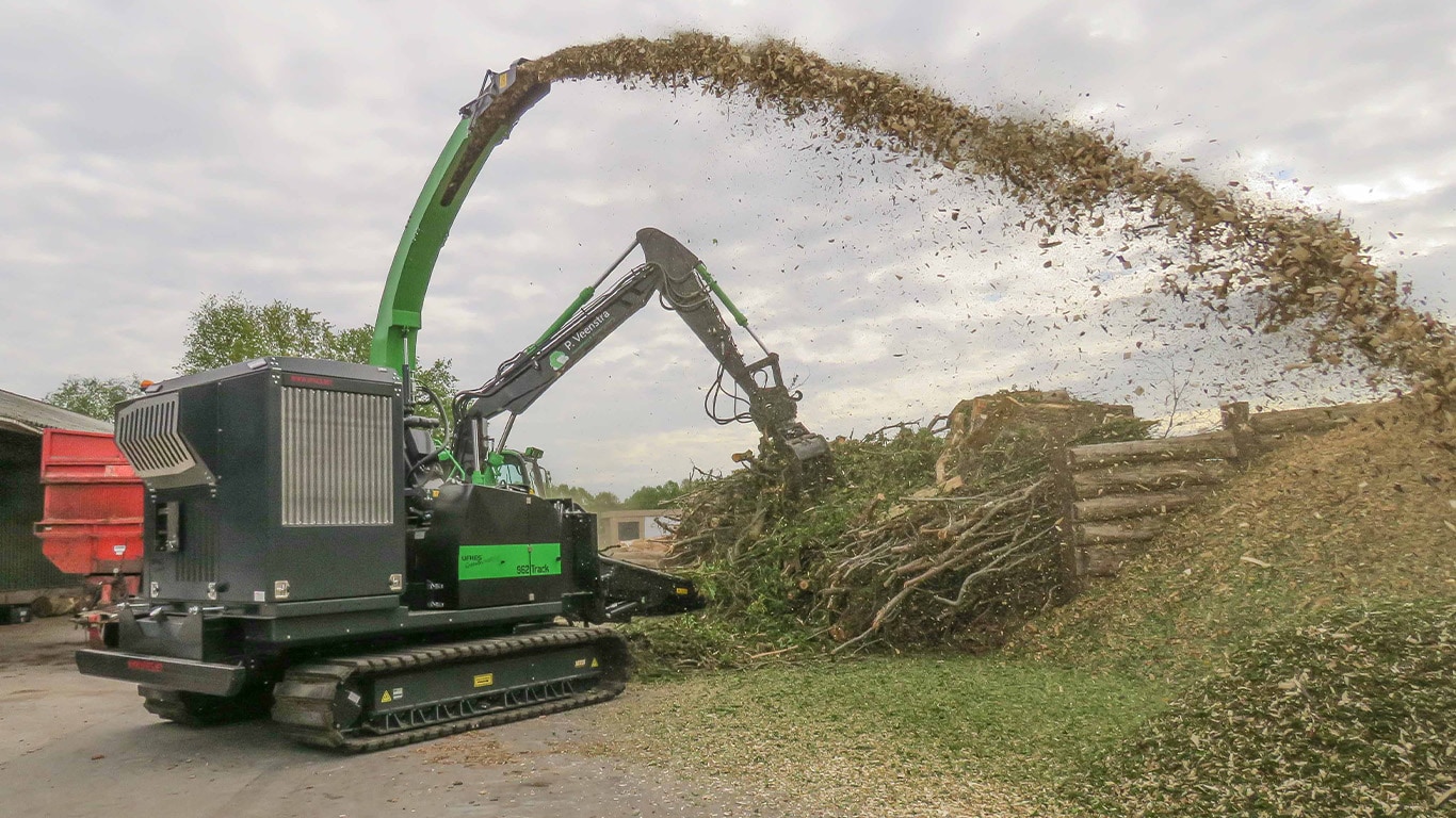 A Ufkes Greentec woodchipper powered by a John Deere industrial engine spraying wood chips onto a large mound of yard waste