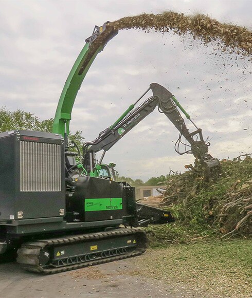 A Ufkes Greentec woodchipper powered by a John Deere industrial engine spraying wood chips onto a large mound of yard waste