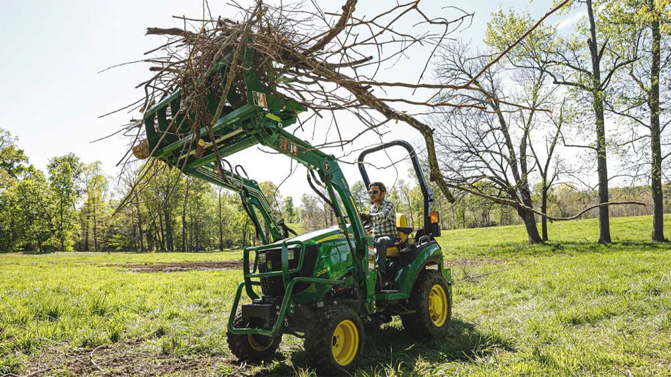 Man holding a pile of sticks in the air using a 2025r tractor