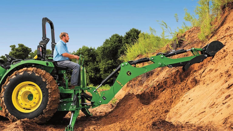 Man driving a 4044r up a hill with an attachment scooping dirt