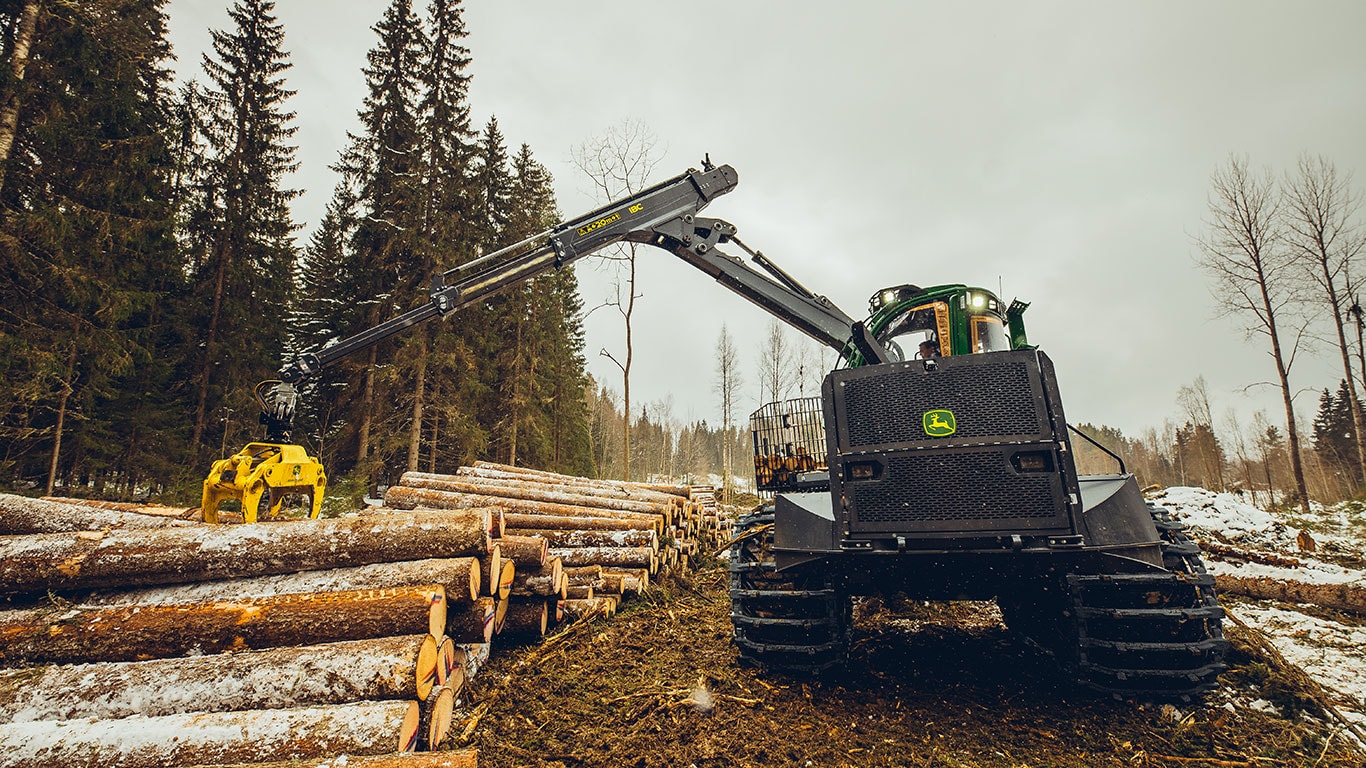 John Deere 2510H forwarder with extended boom in a forested logging area.