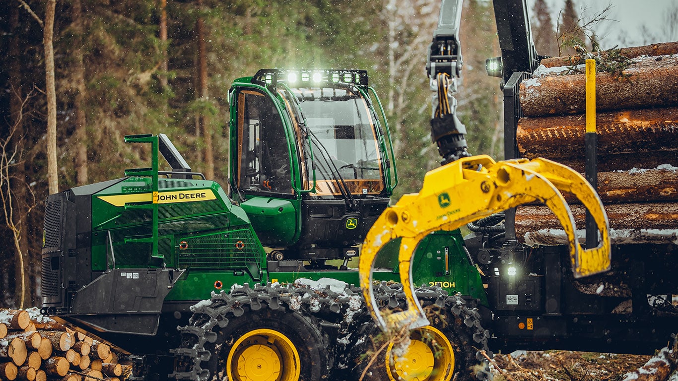 John Deere 2510H forwarder using grapple attachment to lift logs in a forest setting.