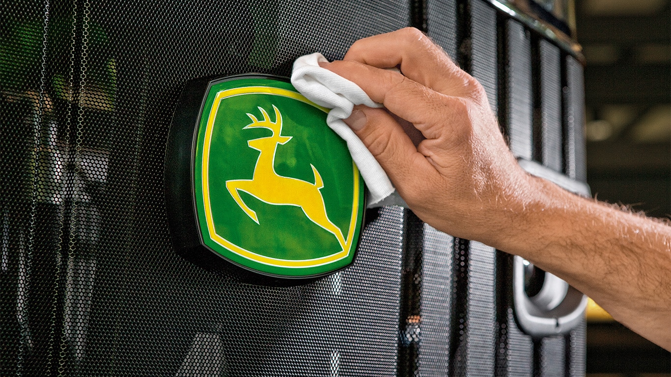 Mano de un hombre limpiando el logo de John Deere en maquinaria agrícola.
