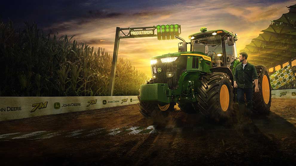 La imagen muestra una máquina John Deere en una carretera, con un hombre de piel clara y cabello negro al lado