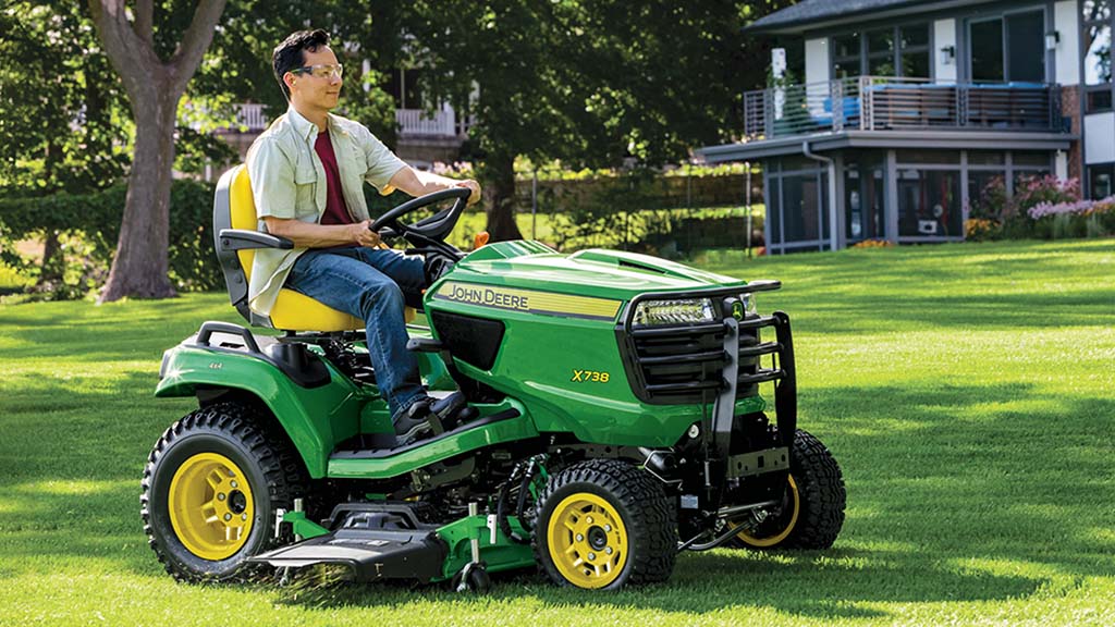A person in safety glasses mowing a backyard on a green riding mower.