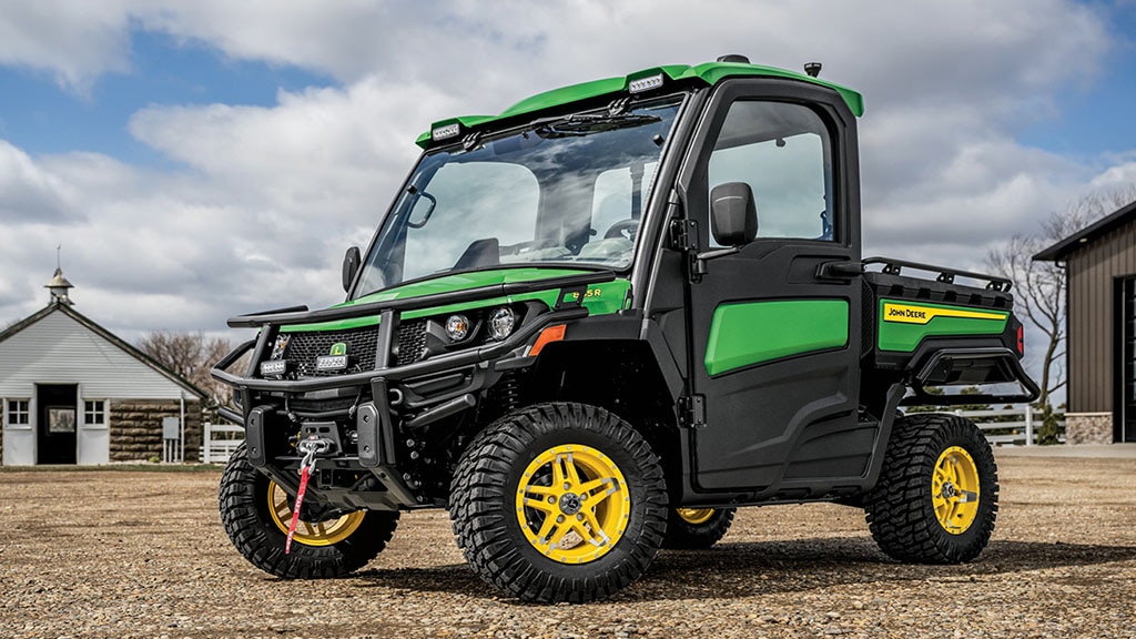 A green Gator XUV sits on gravel in front of some barns.