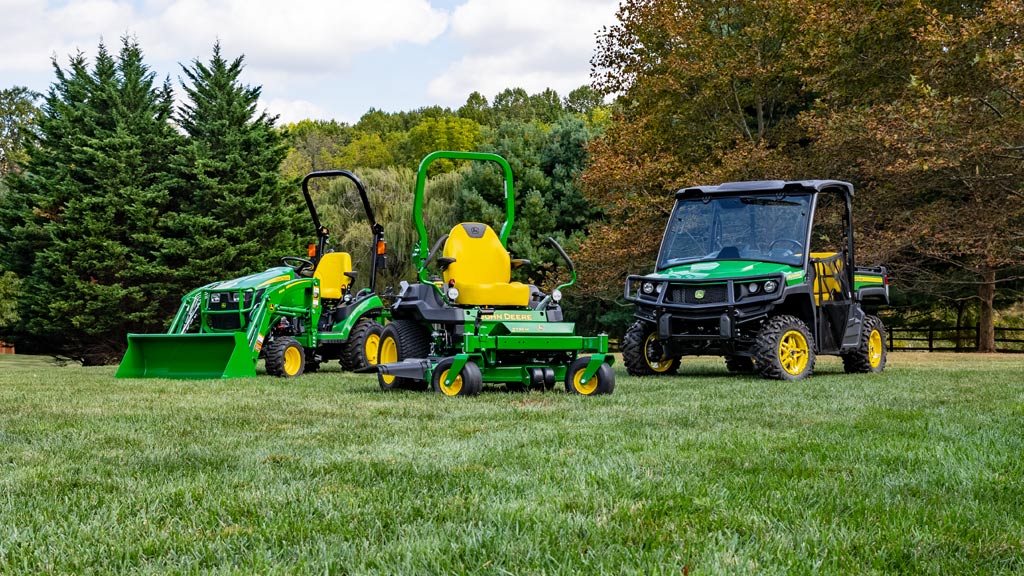 Three different types of John&nbsp;Deere lawn and garden equipment in a field with trees in the background