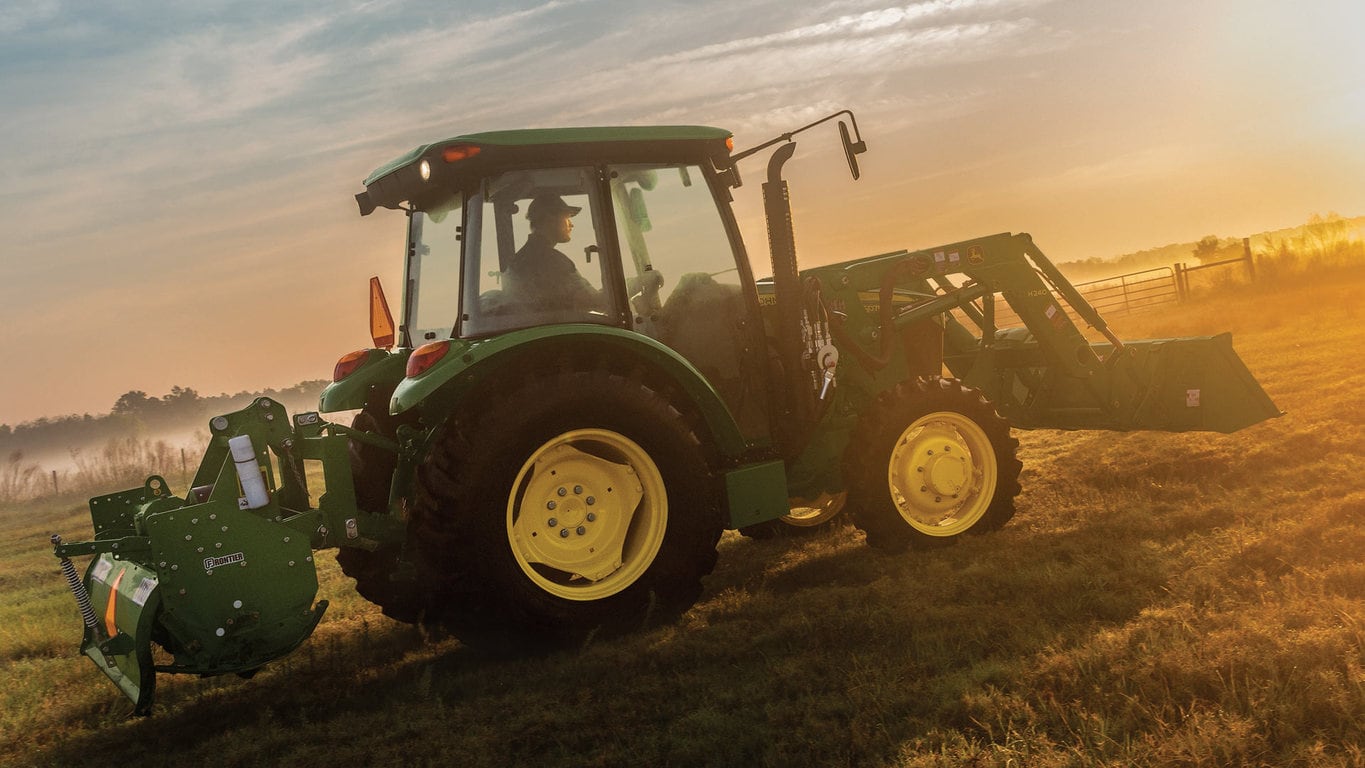 5E Tractor with loader and tiller moving across field at sunrise.