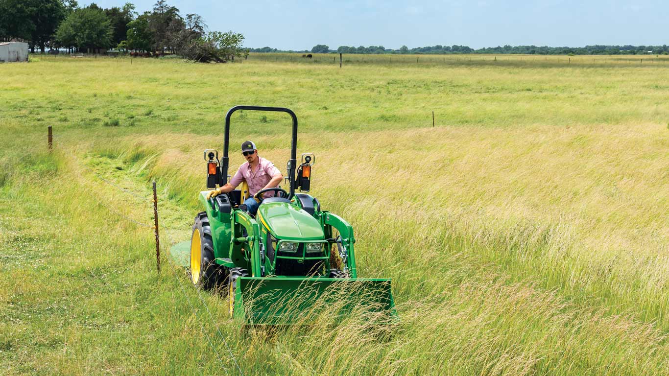 man driving a John Deere 3043D compact tractor in a pasture