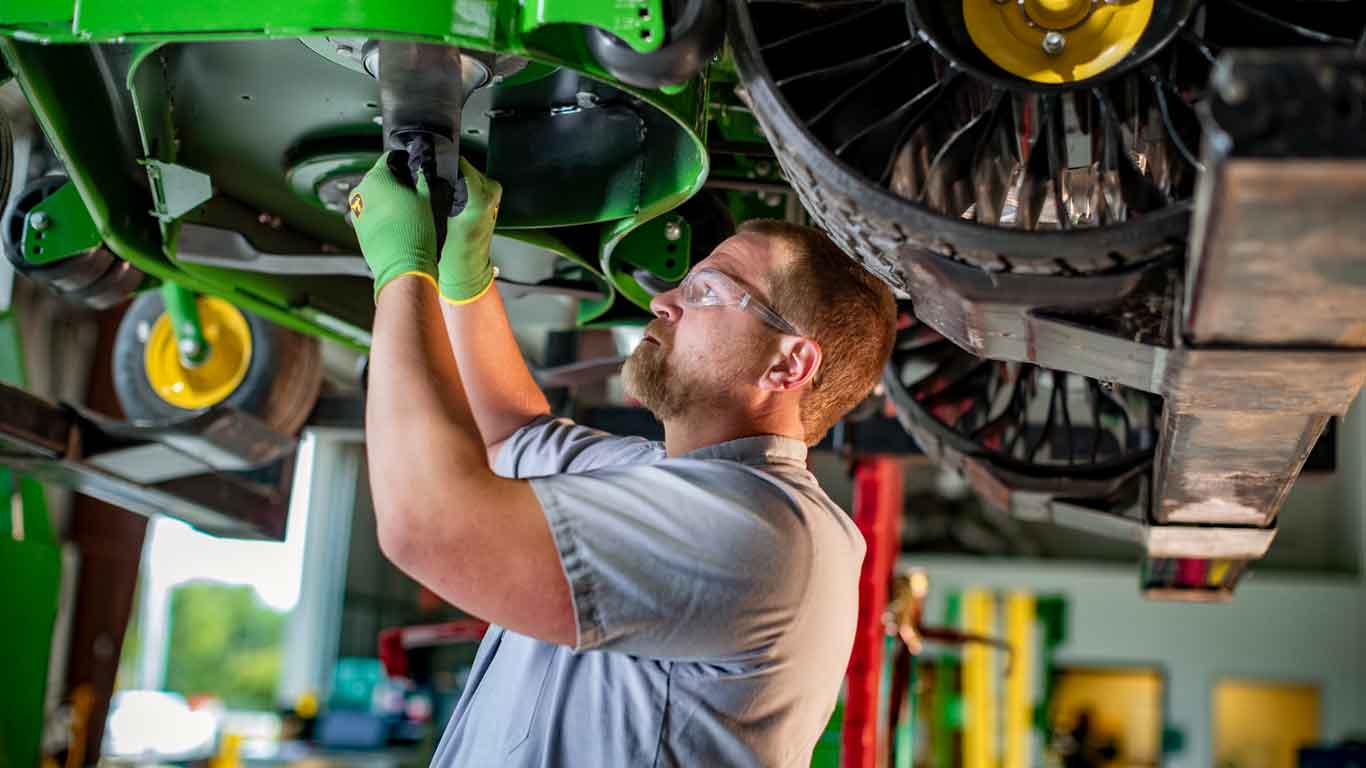 Mechanic with John Deere safety gloves and safety glasses operating under a John Deere mower