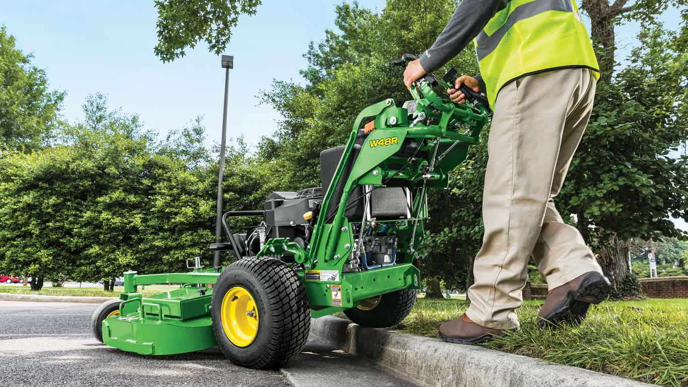 Landscaper going over a curb with a John Deere W48R Commercial Walk Behind Mower