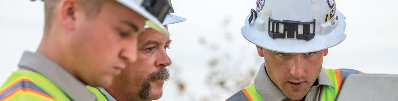   Three people look at a tablet together on a jobsite