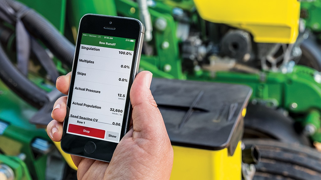 Smartphone showing ag app metrics, with farming equipment in the background.