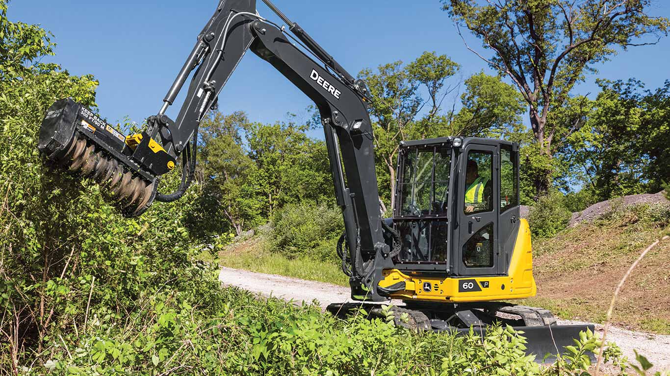 John&nbsp;Deere excavator using a rotary cutting attachment to clear vegetation beside a gravel path.