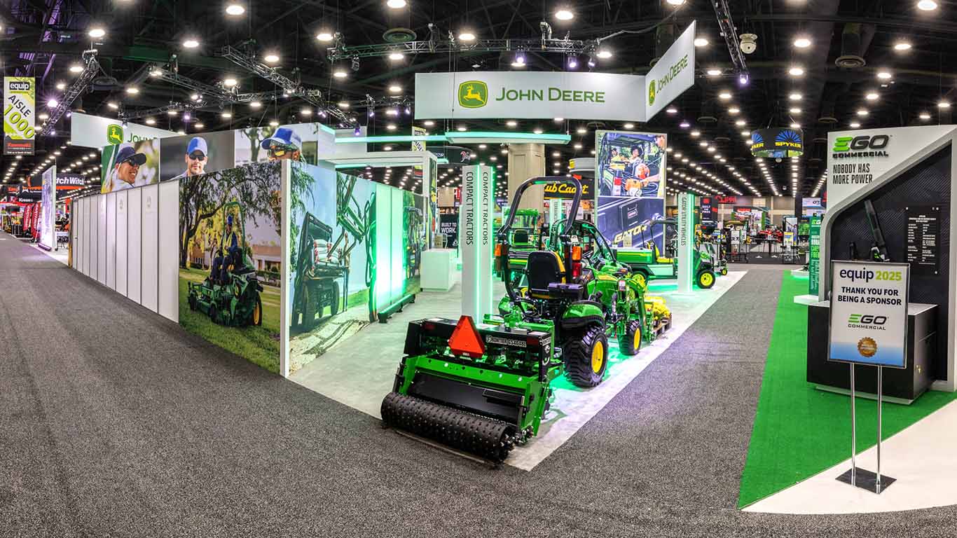 Back shot of the green seeder attached to the Deere compact tractor staged indoors.