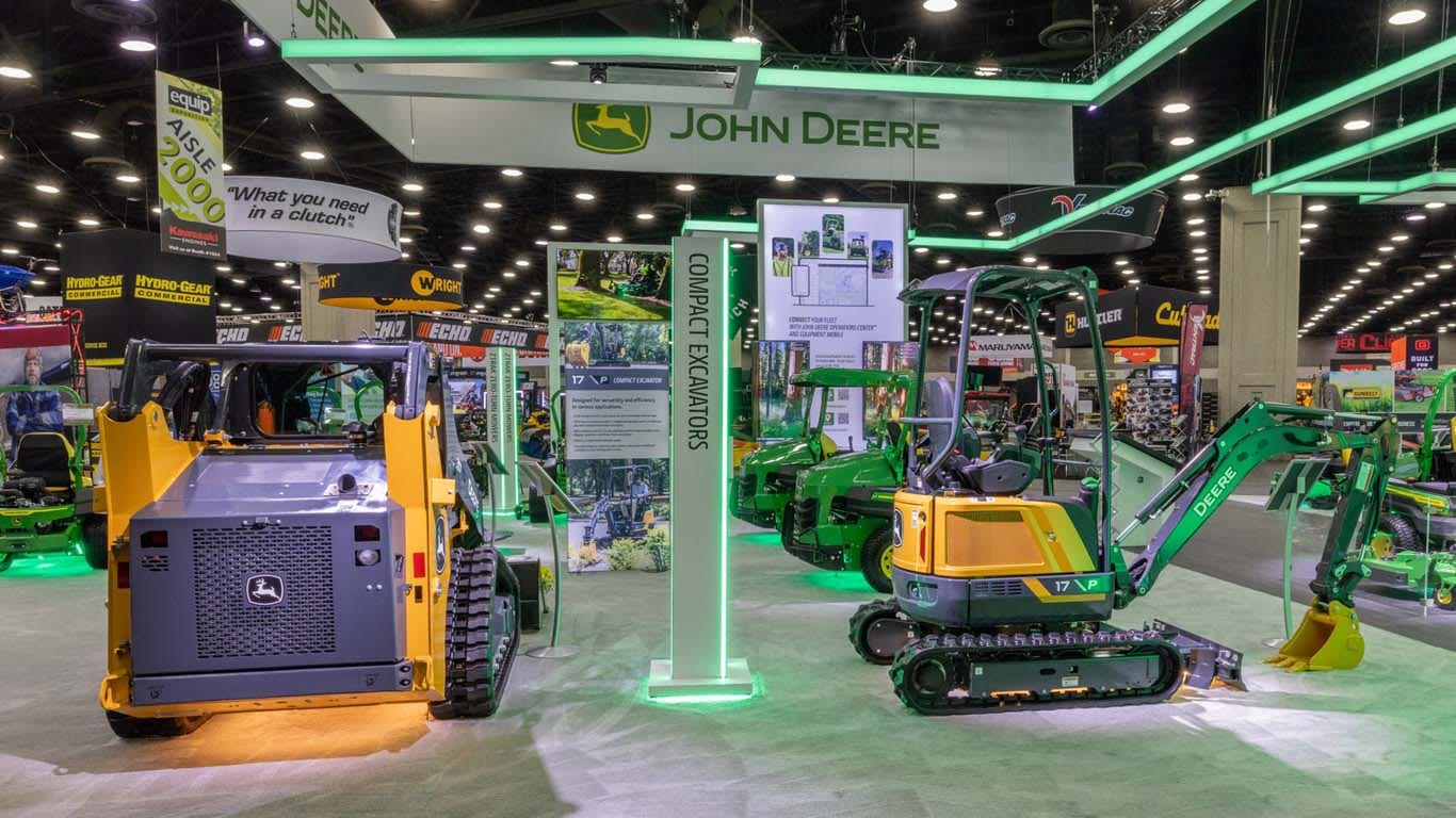 Staged indoors, a yellow mini-excavator and a skid steer rest with yellow under-lighting.
