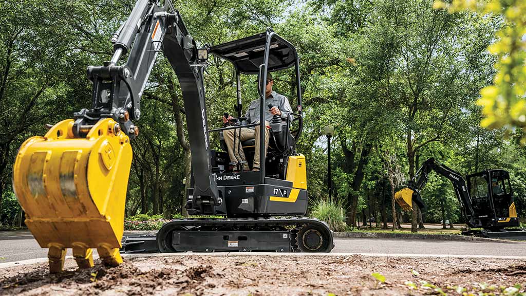 A yellow mini-excavator digging its bucket teeth into the soil of a college campus.