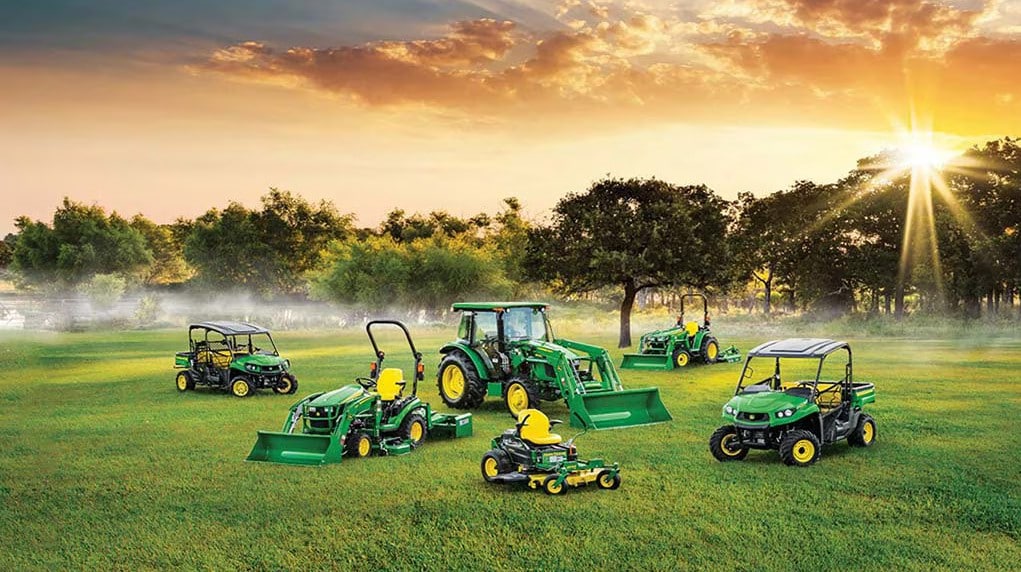 Green Gators, mowers, and tractors in a field during sunrise.