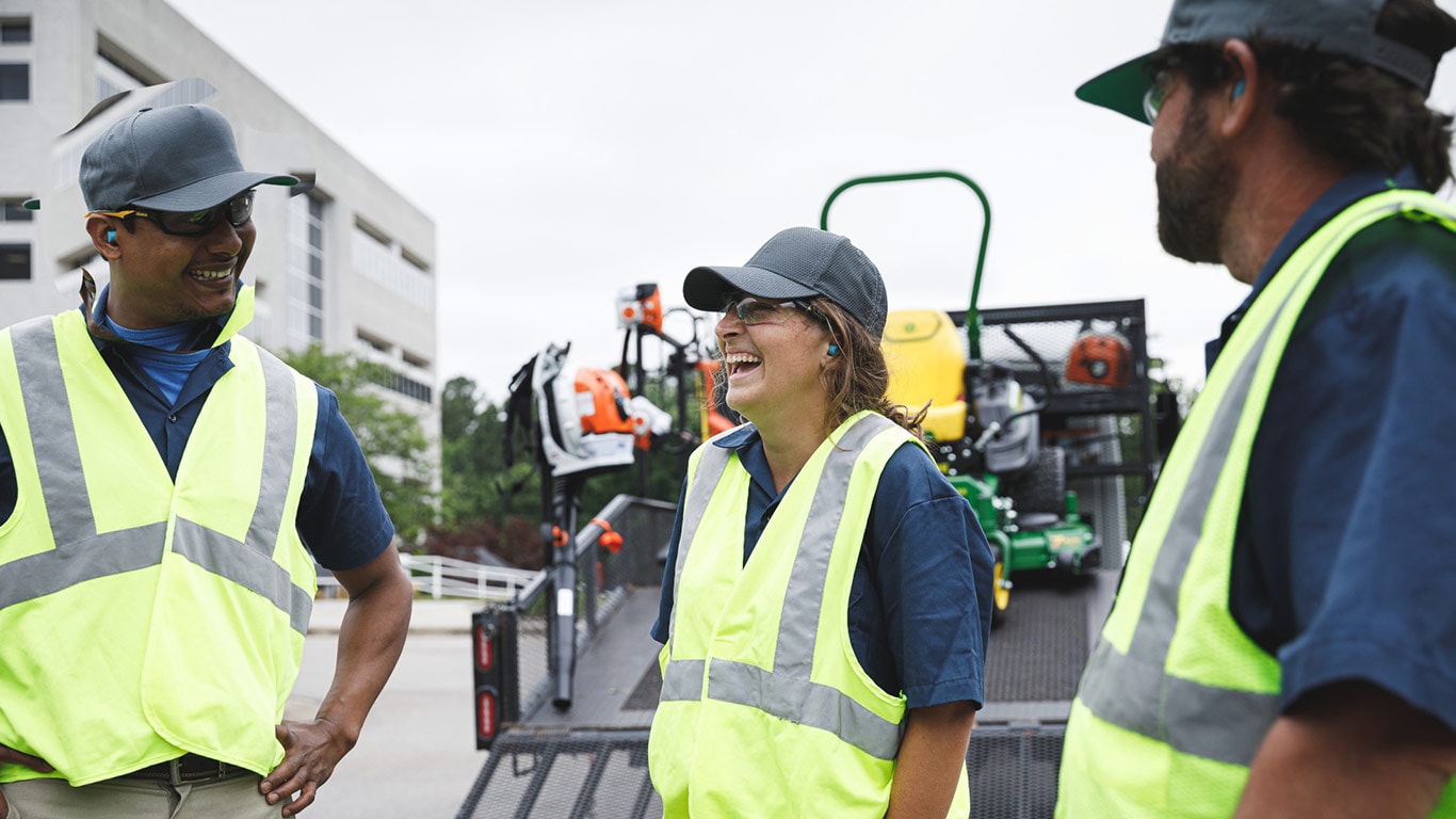 Three landscape professionals talking behind a truck with landscaping equipment.