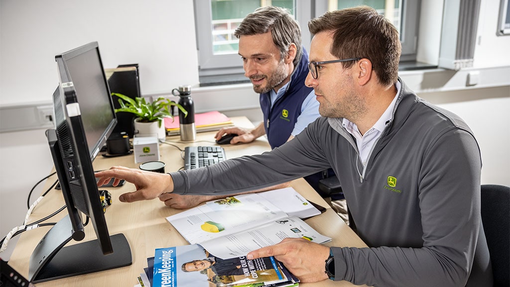 Two people in an office pointing at a monitor display.