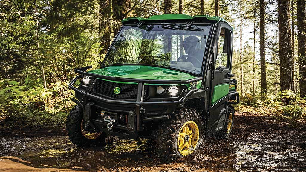A Gator Utility Vehicle crossing a muddy creek in the woods.