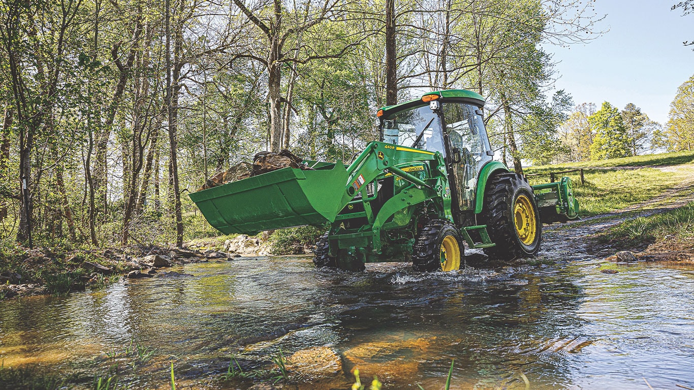 Photo of the 4075R in a pond, scooping rocks into the bucket