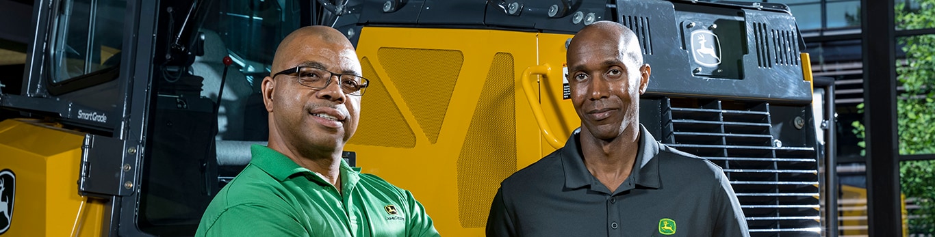 John Deere employees in front of a piece of construction equipment 