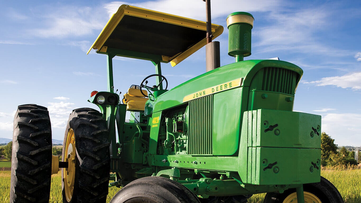 Vintage green John Deere tractor parked in a field under a blue sky.