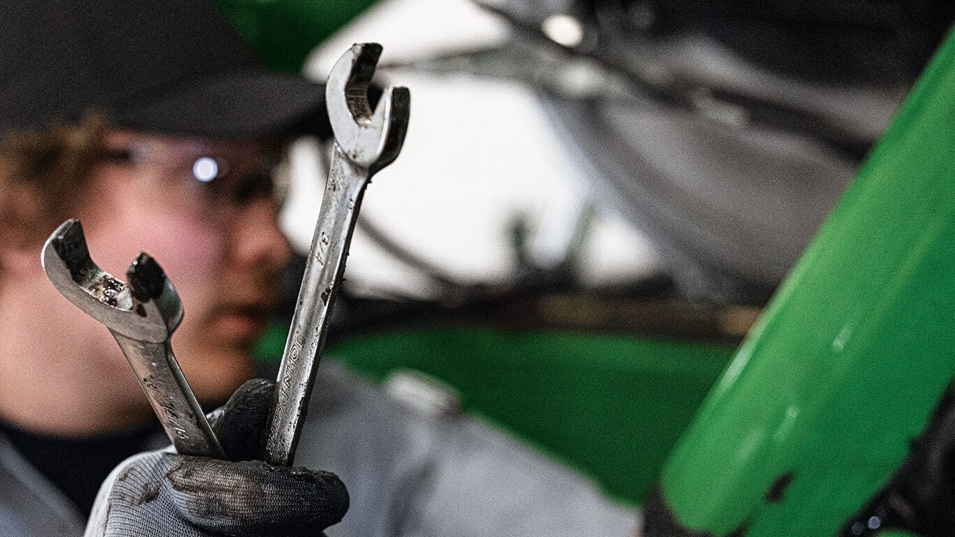 Person using a wrench to work on internal machinery inside a tractor.