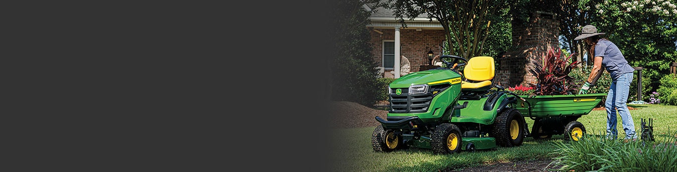 Person in a  garden picking up plants from a cart attached to riding lawn mower