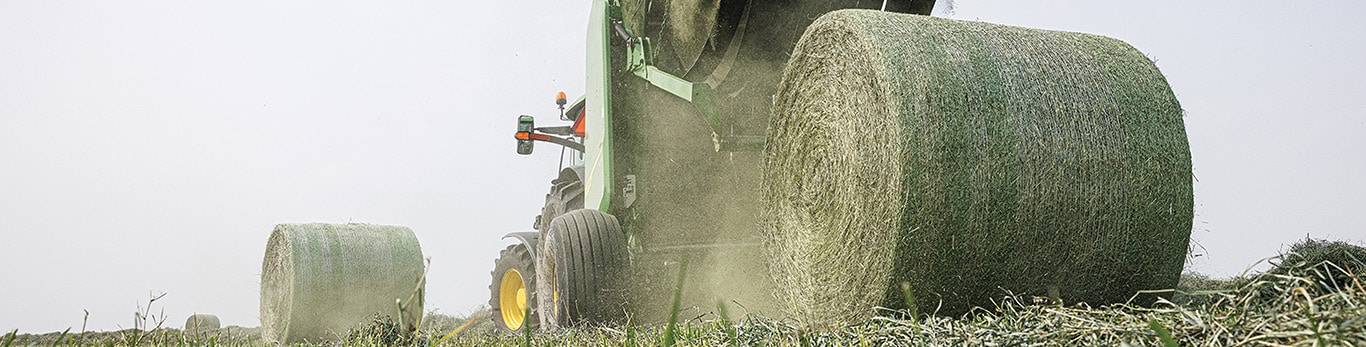 A tractor towing a round baler as a large bale is released onto the field.