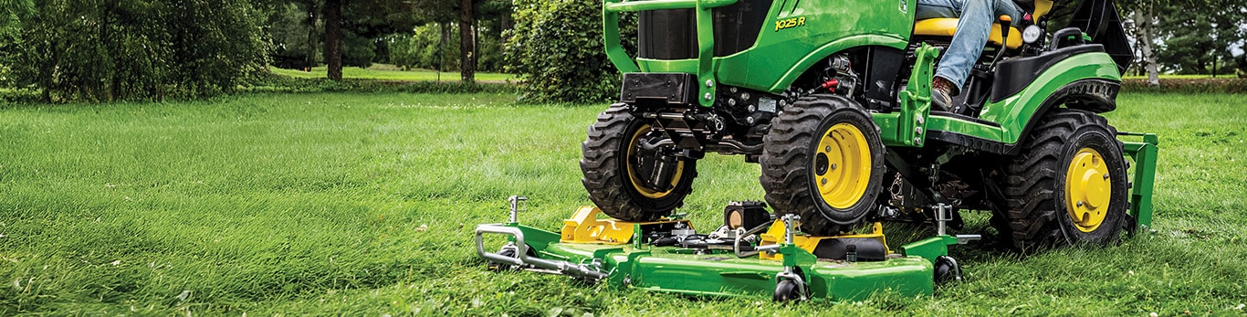 A compact John Deere tractor driving over a quik-knect mower deck attachment on a grassy lawn.