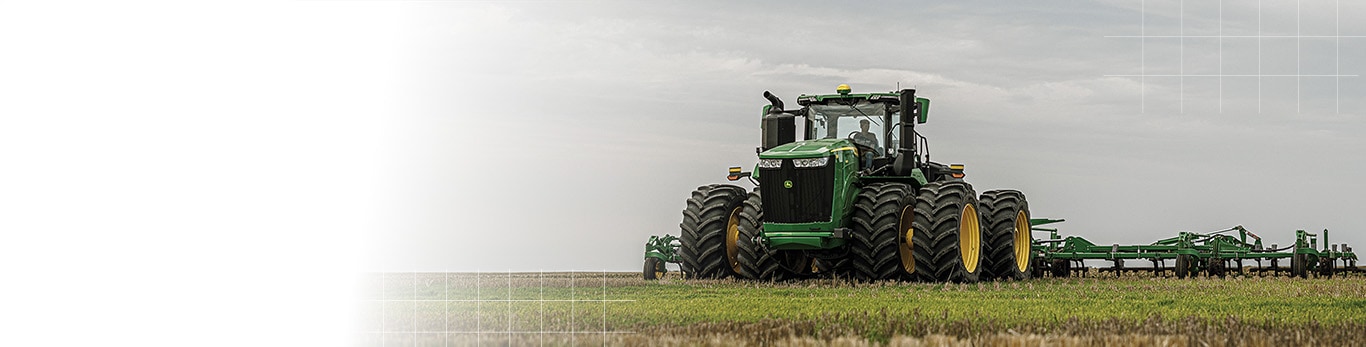 A large John Deere tractor pulling a tillage implement across an open field.