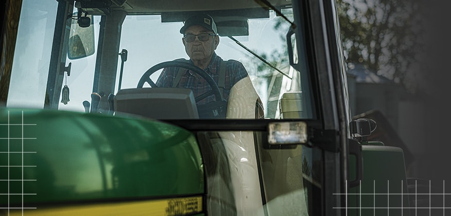 View from outside a tractor cab showing an operator seated at the controls.