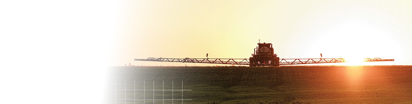 A sprayer with its boom extended across the field at sunrise.