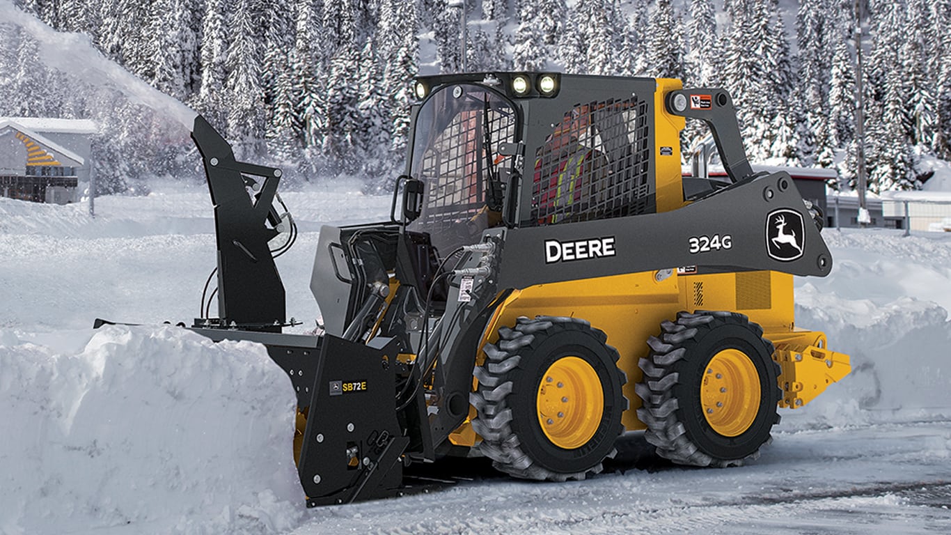 A 324G skid steer with SB72E Snow Blower attachment blowing snow off a road.