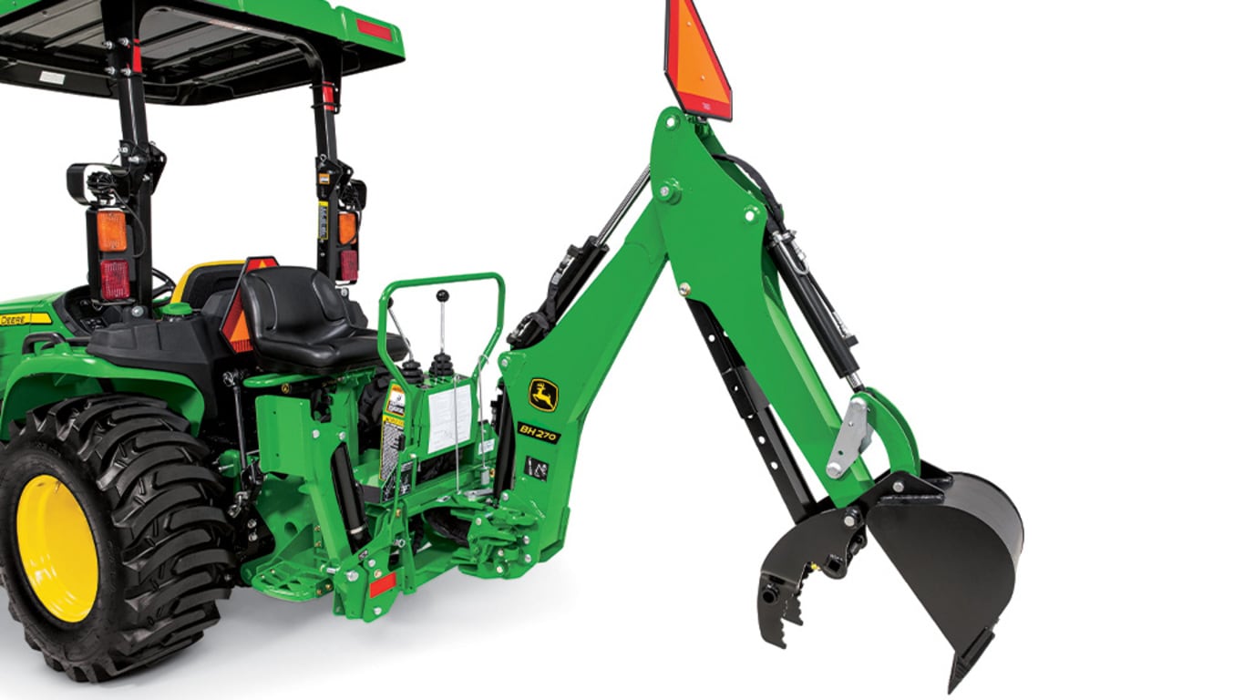 A studio close-up of a green backhoe attached to a Deere compact tractor with the bucket claw open.