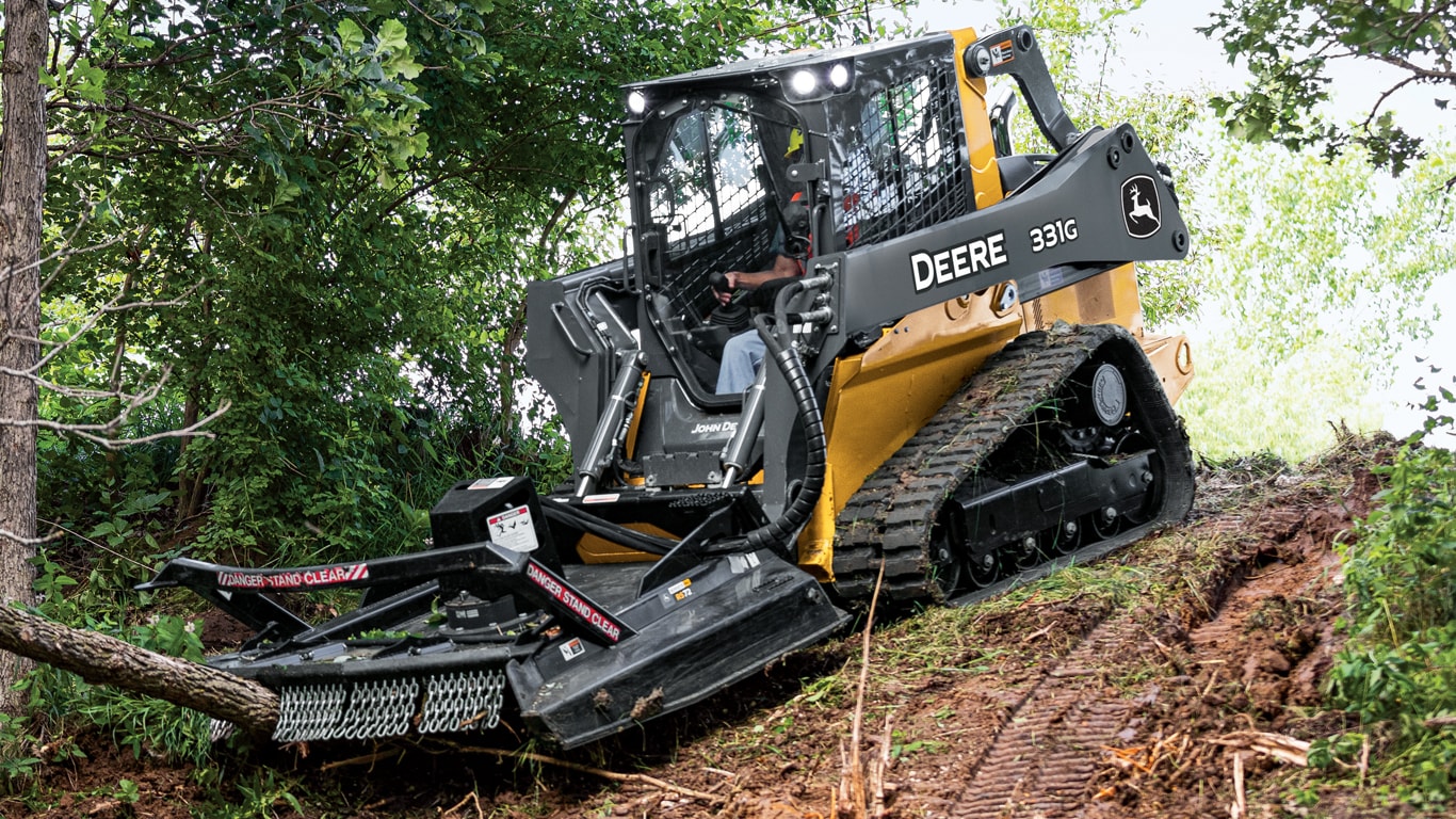 A 331G compact track loader clearing trees and brush with the RS72 Extreme Duty Rotary Cutters attachment.