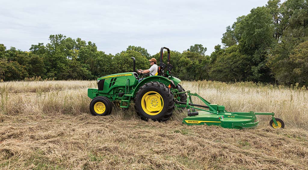 A person driving a compact tractor with a rotary cutter, mowing tall grass in a field