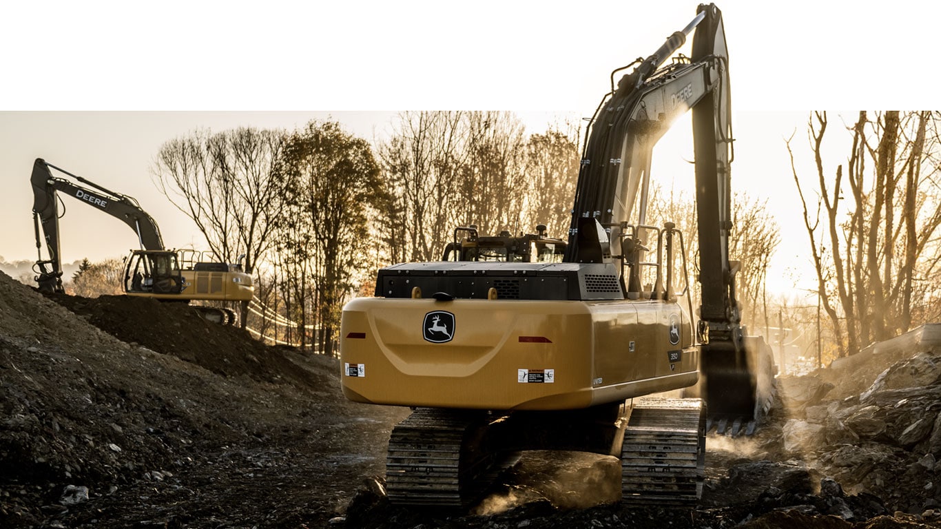 Two John Deere excavators scooping dirt on a jobsite at daybreak.