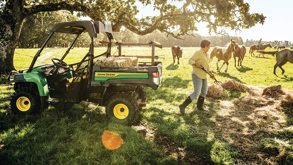 woman shoveling hay into a work series Gator™ in a field