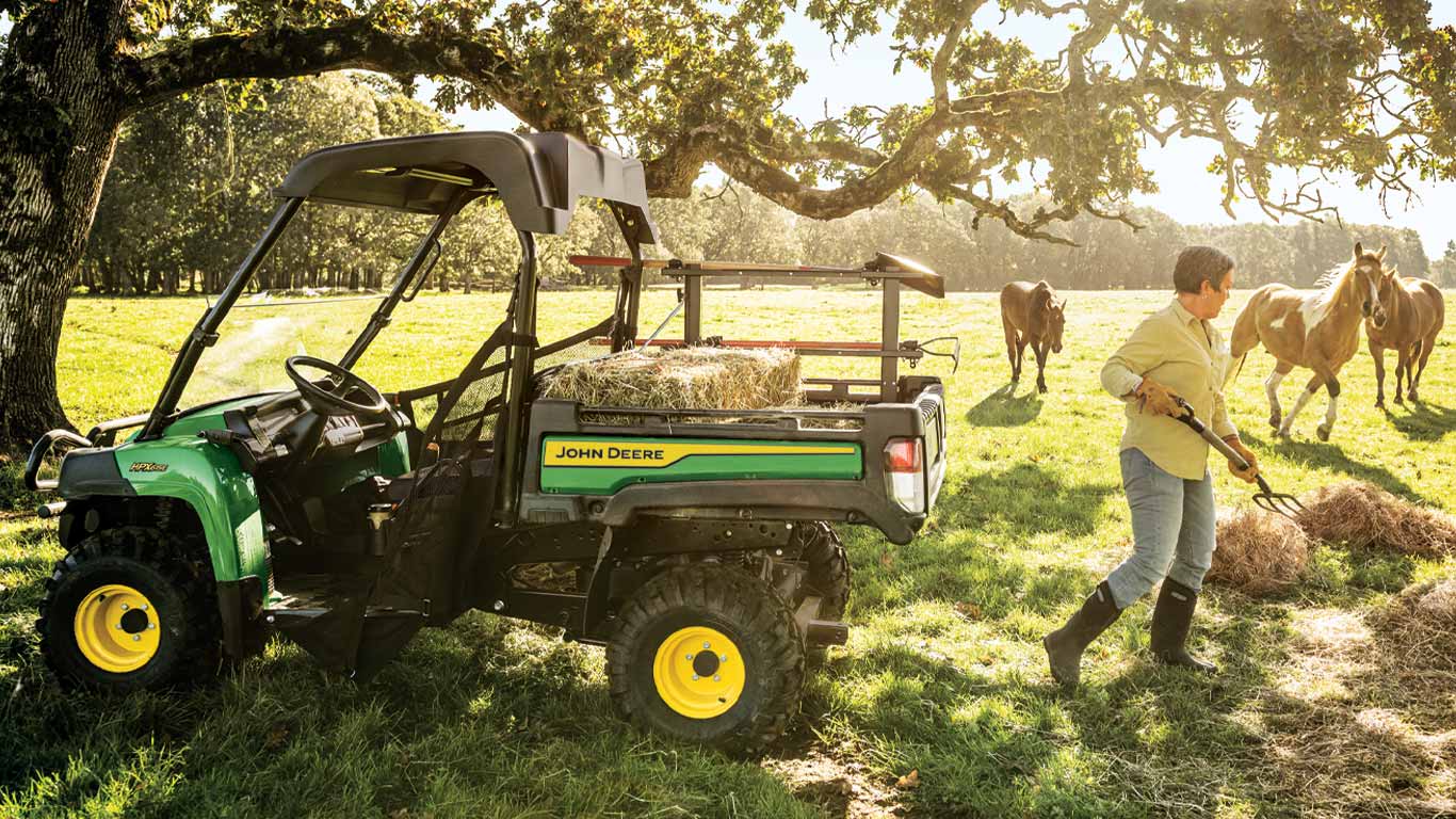 woman shoveling hay into a work series Gator™ in a field