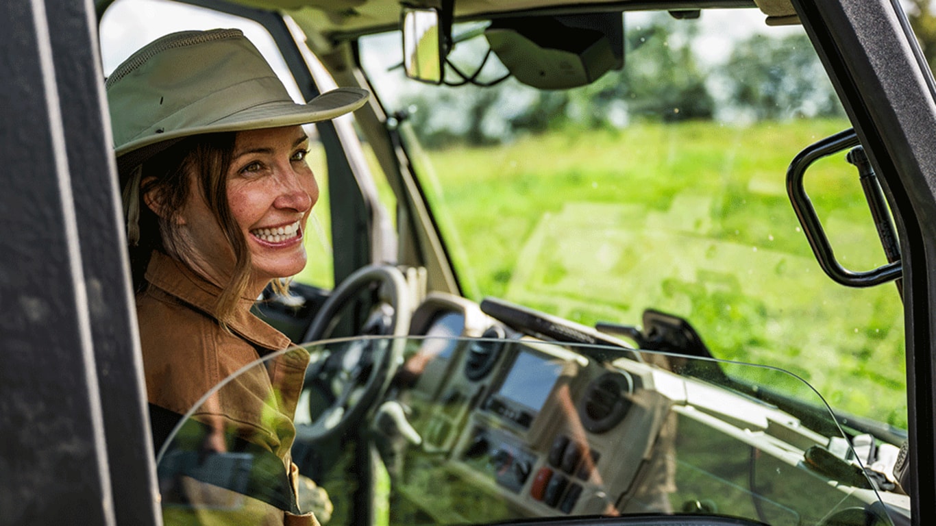 A person in a wide-brimmed hat smiles over the rolled-down window of a cabbed Gator.