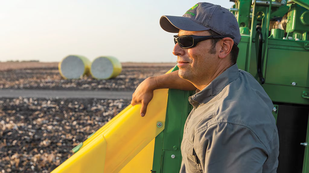 A farmer overseeing the unloading of wrapped, round cotton modules from a tilted truck bed
