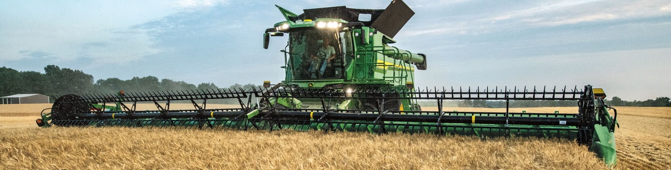 Wide photo form the front of a John Deere S7 Combine harvesting wheat with a draper head