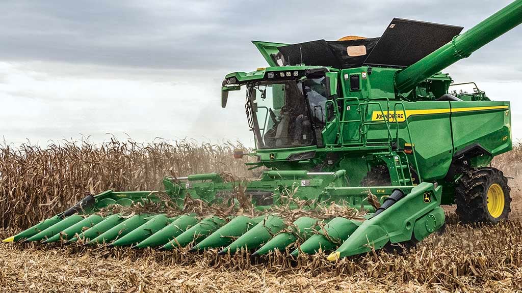 Photo of a John Deere S7 Combine with a corn head, completing a pass in corn
