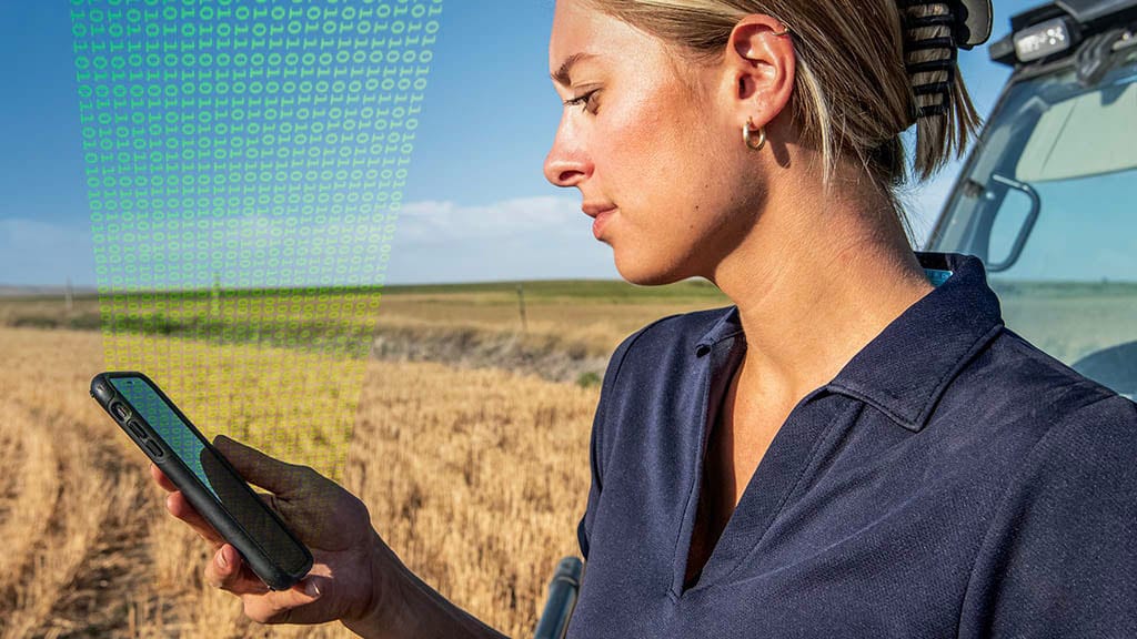 Close-up photo showing a female farmer consulting her mobile device while standing in a partially-harvested field.