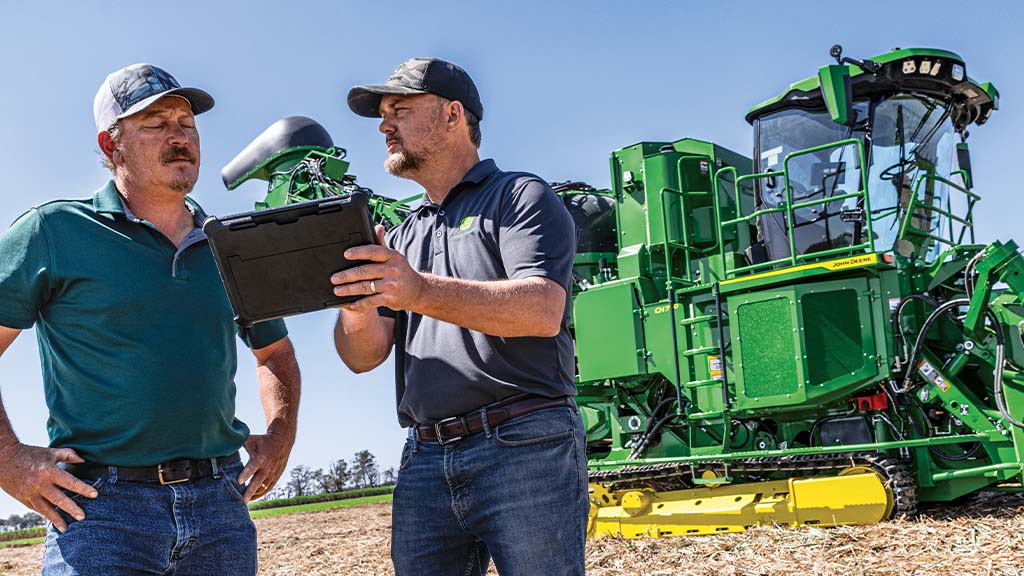 Photo showing two farmers in a field discussing field results on a tablet with a CH Series Sugar Harvester in the background.