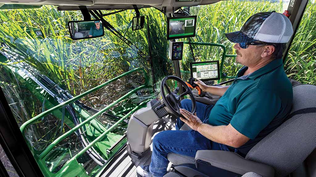 Close-up, in-cab photo showing a farmer operating a CH Series Sugar Harvester, with standing crop visibe throough the cab windows.